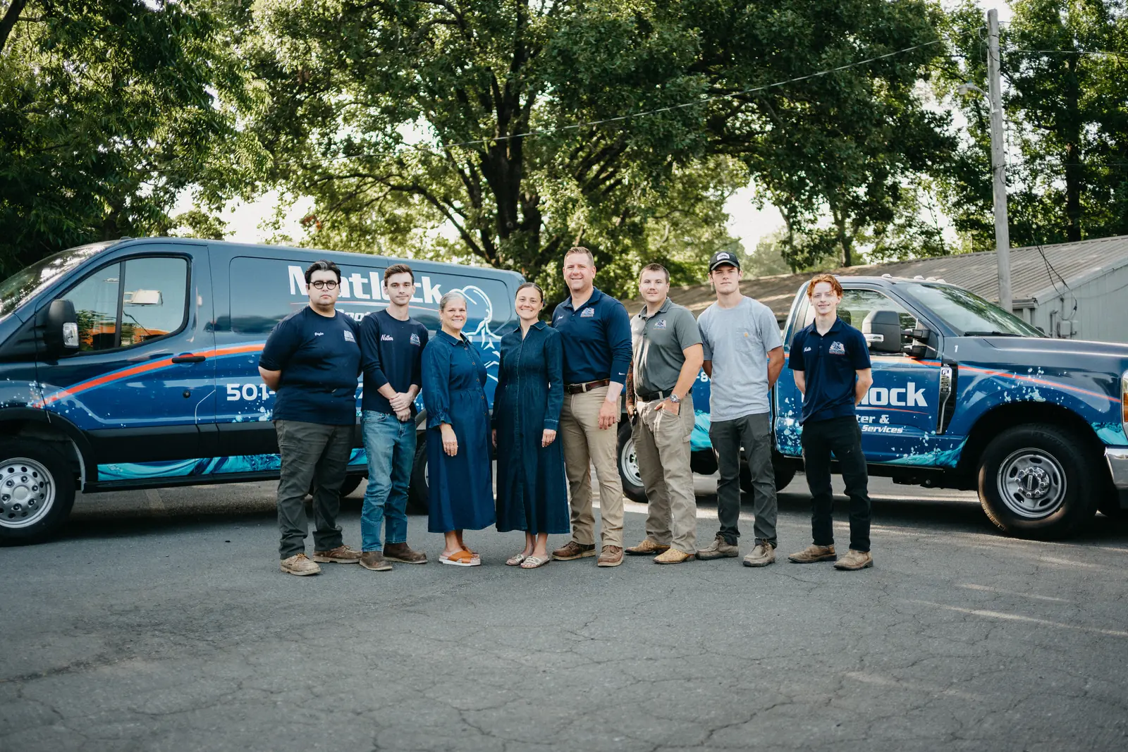 The full Matlock Rooter Services crew standing in front of their wrapped service vans in Sherwood, Arkansas